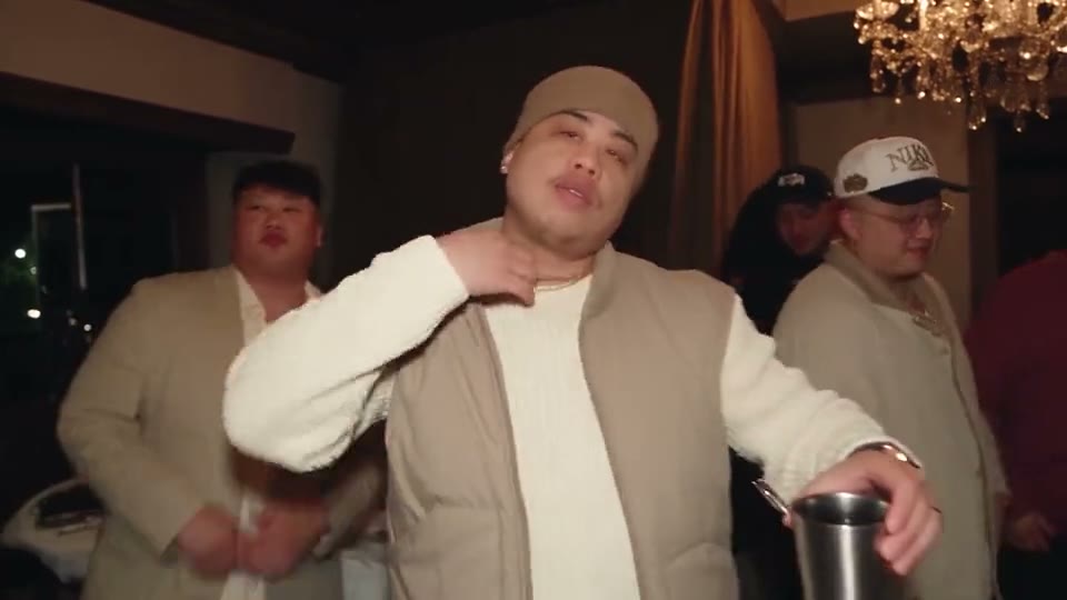 A beige beanie and puffer vest at the center of the party, cup raised, the crew behind him.
