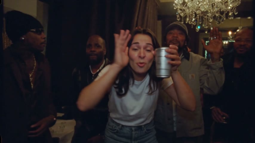 A woman in a white tee leads the party under the chandeliers, cup in hand, the crew behind her.