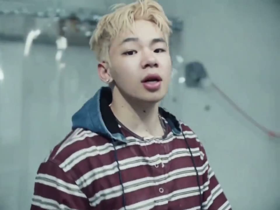 A friend with bleached hair raps in a striped shirt, then a blue zip hoodie, as the camera circles the boxes. Made with AI by the friend and shown with permission.